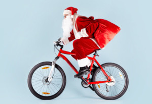 Photo of happy Santa Claus with red sack riding bike
